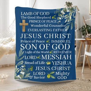May include: A blue throw blanket with a white floral design and white text. The text reads: 'LAMB OF GOD', 'The Good Shepherd', 'PRINCE OF PEACE', 'Wonderful Counselor', 'EVERLASTING FATHER', 'JESUS CHRIST', 'Prince of Peace', 'IMMANUEL', 'SON OF GOD', 'Light of the World', 'REDEEMER', 'LORD', 'MESSIAH', 'Bread of Life', 'YESHUA', 'JESUS CHRIST', 'LORD', 'Mighty', '& Savior', 'GOD'.