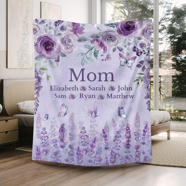 May include: A lavender-colored blanket with the word "Mom" in the center, surrounded by floral and butterfly designs. The names Elizabeth, Sarah, John, Sam, Ryan, and Matthew are listed below "Mom".