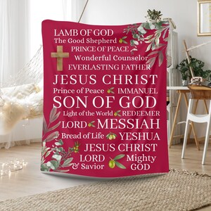 May include: A red tapestry with white text and green olive branches. The text reads "Lamb of God, The Good Shepherd, Prince of Peace, Wonderful Counselor, Everlasting Father, Jesus Christ, Prince of Peace, Immanuel, Son of God, Light of the World, Redeemer, Lord, Messiah, Bread of Life, Yeshua, Jesus Christ, Lord, Mighty, & Savior, God."