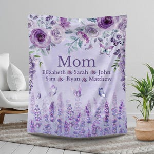 May include: A personalized lavender-colored blanket with the word "Mom" in large letters. The blanket features floral and butterfly designs, with names below the word "Mom". The blanket is decorated with purple roses and lavender.