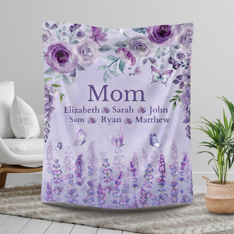 May include: A personalized lavender-colored blanket with the word "Mom" in large letters. The blanket features floral and butterfly designs, with names below the word "Mom". The blanket is decorated with purple roses and lavender.