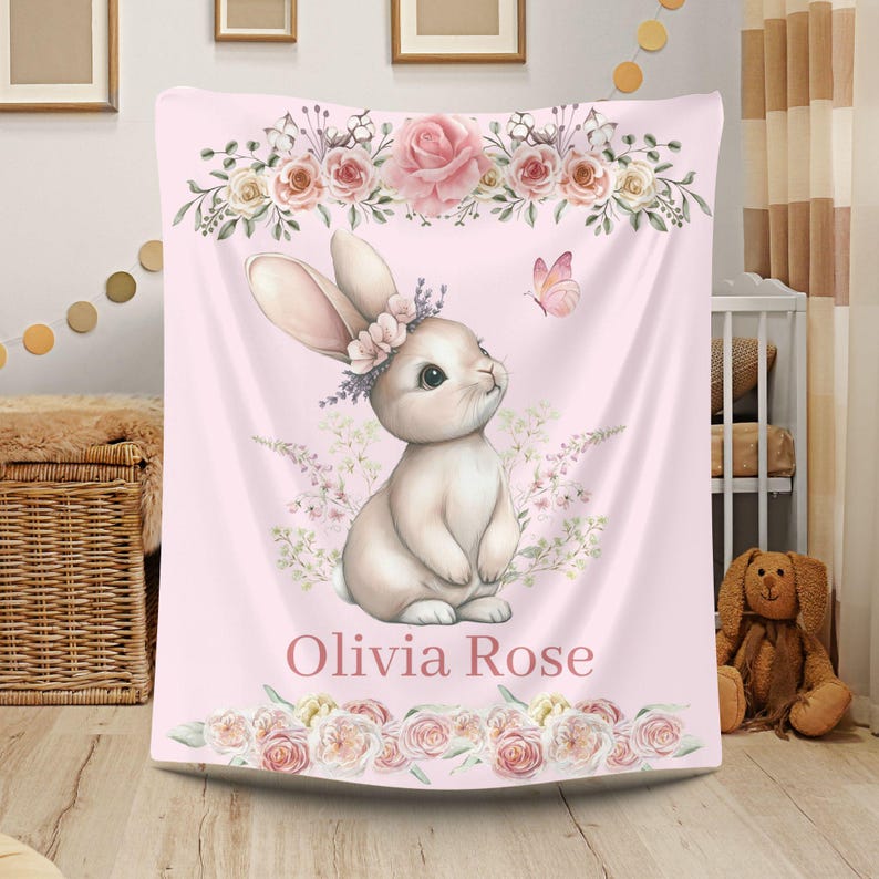 Peut inclure: Couverture rose pour b&eacute;b&eacute; avec une illustration &agrave; l'aquarelle d'un lapin portant une couronne de fleurs, avec un papillon et des motifs floraux. Le nom "Olivia Rose" est imprim&eacute; en bas. La couverture est orn&eacute;e de roses et d'autres fleurs.