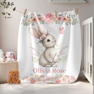 Peut inclure: Couverture de b&eacute;b&eacute; blanche avec une illustration &agrave; l'aquarelle d'un lapin portant une couronne de fleurs et un papillon rose. La couverture est orn&eacute;e de roses roses et du nom "Olivia Rose".