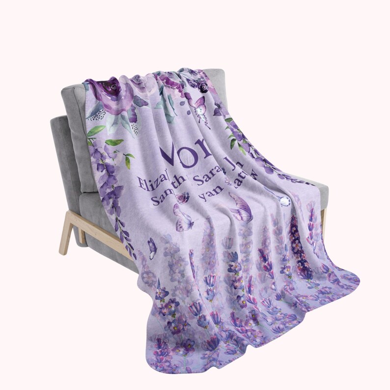 May include: A light purple throw blanket draped over a gray armchair. The blanket features floral and butterfly designs in shades of purple and white, with the names "Eliza", "Sarah", and "Jan" printed on it.