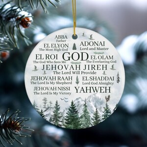 May include: A round white ceramic ornament featuring a gold hanging string. The surface displays black text listing various names of God, including Abba, El Elyon, Adonai, El Roi, El Olam, Jehovah Jireh, Jehovah Raah, El Shaddai, Jehovah Nissi, and Yahweh.