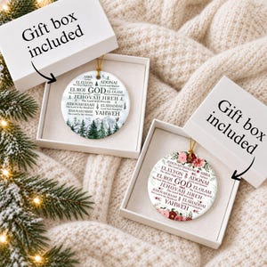 May include: Two round white ceramic ornaments in open gift boxes. One ornament features a green pine forest graphic, the other a floral design. Both display the text GOD and various names like JEHOVAH JIREH, EL SHADDAI, and YAHWEH with meanings.