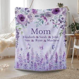 May include: A lavender-colored blanket with floral and butterfly designs. The blanket features the word "Mom" in the center, with names below. The top border has purple roses and greenery, and the bottom has lavender flowers.