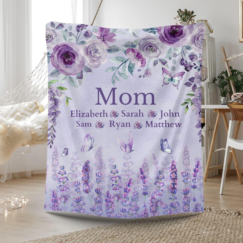 May include: A lavender-colored blanket with floral and butterfly designs. The blanket features the word "Mom" in the center, with names below. The top border has purple roses and greenery, and the bottom has lavender flowers.