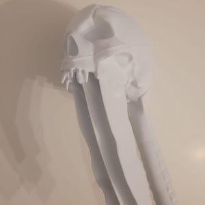 Puede incluir: Una máscara de calavera de tela blanca con dientes afilados y largas tiras de tela que fluyen. La máscara tiene un diseño de calavera detallado con cuencas de los ojos y una mandíbula definida. La tela parece suave y drapeada.