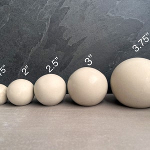 Puede incluir: Cinco esferas blanquecinas de varios tama&ntilde;os, que van desde 4,4 cm a 9,5 cm de di&aacute;metro, est&aacute;n dispuestas en fila. Las esferas son lisas y tienen un acabado mate. La imagen est&aacute; sobre un fondo gris oscuro.