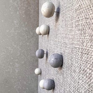 May include: A set of six round concrete knobs in various sizes, with a speckled finish, mounted on a textured wall.