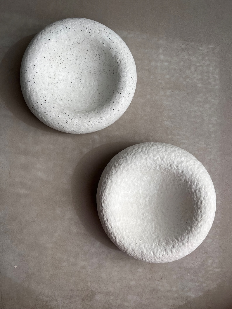 May include: Two white ceramic bowls with a textured surface. The bowls have a rounded shape and a slight indentation in the center.