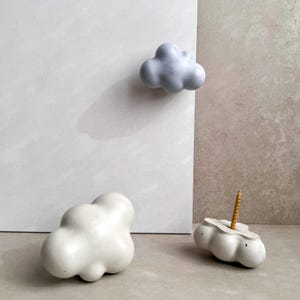 May include: Three concrete cloud-shaped wall hooks, two in white and one in light blue. The hooks are designed to be mounted on a wall.