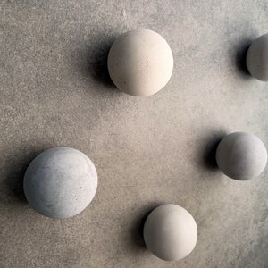 May include: Five round, gray concrete spheres of varying sizes are arranged on a gray textured surface.