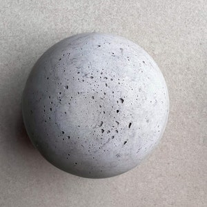 May include: A round, gray concrete sphere with a rough, textured surface.