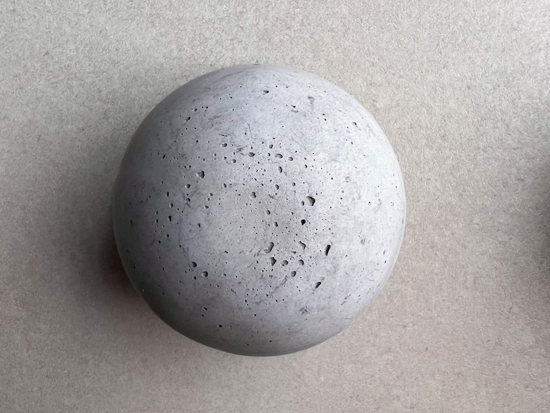 May include: A round, gray concrete sphere with a rough, textured surface.