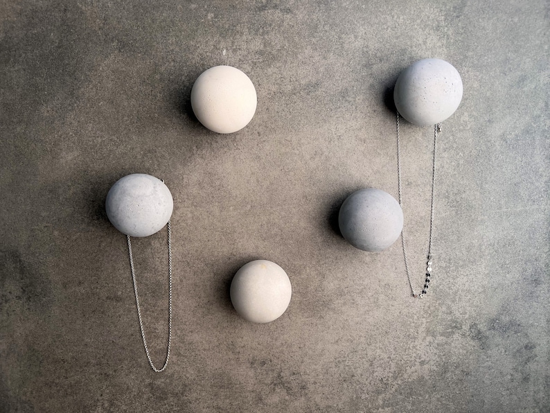May include: Five round concrete wall hooks in white and gray, with a silver chain hanging from one of the gray hooks.