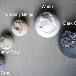 Puede incluir: Vista cenital de cinco esferas en tonos grises, blancos y beige. Cada esfera presenta una superficie texturizada e irregular. Las esferas est&aacute;n etiquetadas como "Creamy Beige", "White", "Dark Gray", "Creamy Gray" y "Bluish Gray".
