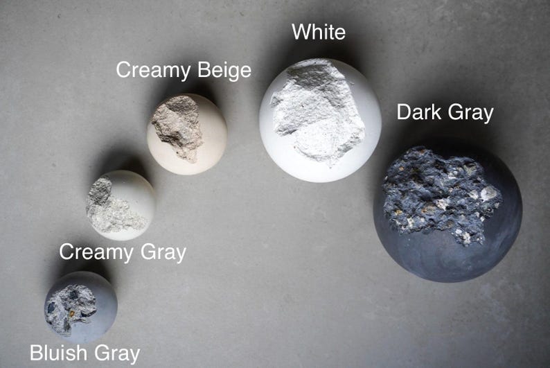 Puede incluir: Vista cenital de cinco esferas en tonos grises, blancos y beige. Cada esfera presenta una superficie texturizada e irregular. Las esferas est&aacute;n etiquetadas como "Creamy Beige", "White", "Dark Gray", "Creamy Gray" y "Bluish Gray".
