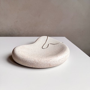 May include: A white ceramic dish with a textured surface, shaped like a melted blob, with a silver chain necklace resting inside.