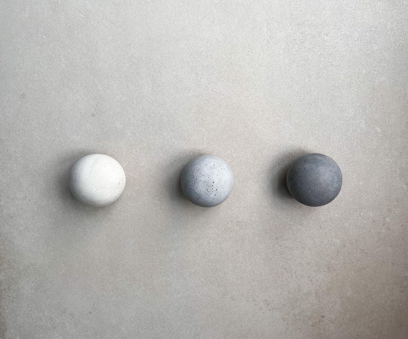 May include: Three round concrete knobs in different shades of gray. The knobs are arranged in a row from left to right, with the lightest shade on the left and the darkest shade on the right.
