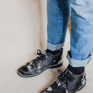 Puede incluir: Un par de zapatos de cordones de cuero de vaca blanco y negro con suela de goma negra.