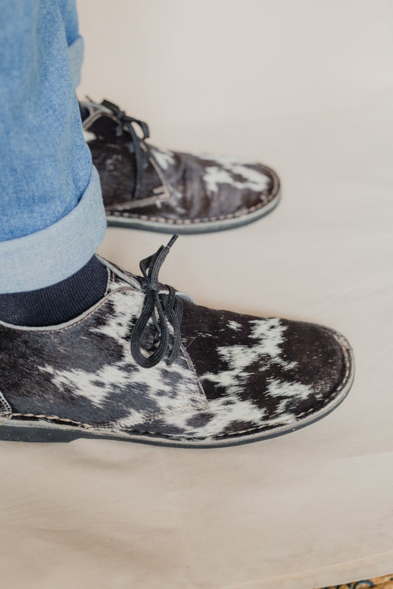 Puede incluir: Un par de zapatos de cordones de cuero de vaca negro y blanco. Los zapatos tienen una suela de goma negra y un cord&oacute;n negro.
