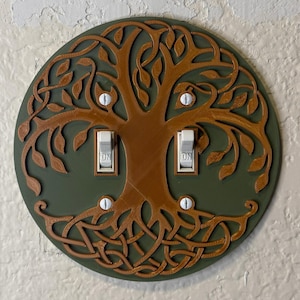May include: A decorative light switch cover featuring a tree of life design. The cover is circular, with a dark green background and a brown tree design. The switches are labeled "ON".