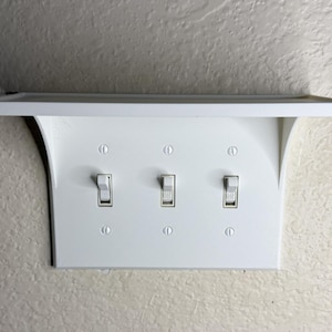 May include: A white light switch plate with three toggle switches and a small shelf above. The switches are in the on position. The word "ON" is visible on the middle switch.