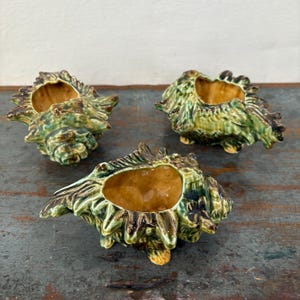 May include: Three ceramic seashell-shaped planters in shades of green and brown. The planters have a textured surface and are designed to resemble seashells.