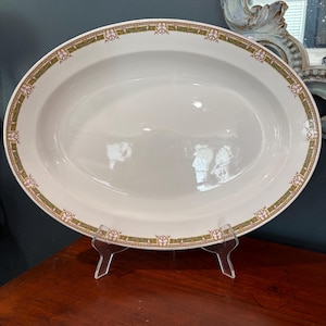 May include: An oval-shaped white ceramic serving platter featuring a decorative border pattern. The rim is adorned with a repeating design of green and gold geometric lines interspersed with small purple floral accents along the entire edge.