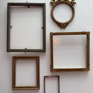 May include: An assortment of antique picture frames in various shapes and sizes. The frames are made of metal and wood, with ornate detailing and a vintage aesthetic. Includes a round frame with cherub accents.