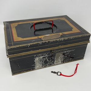 May include: A vintage black metal cash box with a red handle and key. The box has gold and red trim around the top and shows signs of wear. The key is attached to a red string.