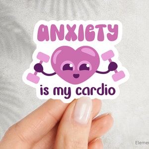 May include: A sticker with the text "ANXIETY is my cardio" in purple. The design features a smiling heart holding dumbbells. The sticker is held by a hand against a light background.
