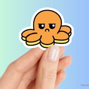 May include: An orange octopus sticker with a grumpy expression. The octopus has eight tentacles with yellow accents and a black outline. The sticker is held between two fingers against a gradient blue and green background.