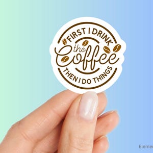 May include: A white, circular sticker with brown text that reads "FIRST I DRINK the Coffee THEN I DO THINGS." The word "Coffee" is in a cursive font. Coffee bean illustrations are included.