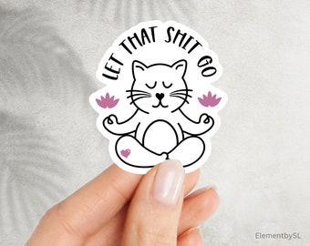 May include: White cat meditating with closed eyes and a peaceful expression. The cat is sitting in a lotus position with pink flowers on either side. The text "Let That Shit Go" is written in a circle around the cat.