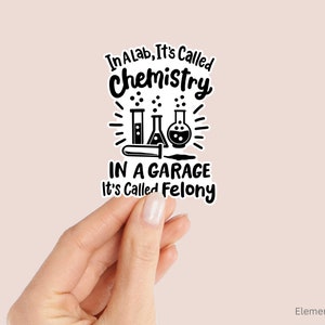 May include: Black and white sticker with the text "In a lab, it's called chemistry. In a garage, it's called felony." with a drawing of beakers and a test tube.