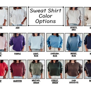May include: A chart showing 14 different color options for a sweatshirt. The colors include white, ash, sports grey, sand, light pink, purple, light blue, carolina blue, indigo blue, navy, red, maroon, military green, forest green, dark chocolate, and black.