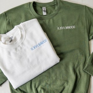 May include: Two sweatshirts, one white and one green, with the same Roman numeral date embroidered on each. The date is II.XVI.MMXXI.