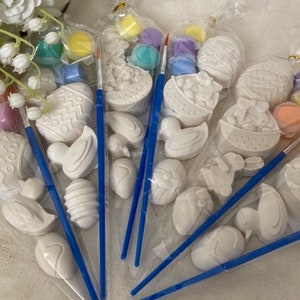 May include: Four sets of Easter-themed paint-your-own ceramic ornaments. Each set includes a small paintbrush, four paint pots in various colours, and a variety of ceramic shapes, including eggs, bunnies, and baskets.