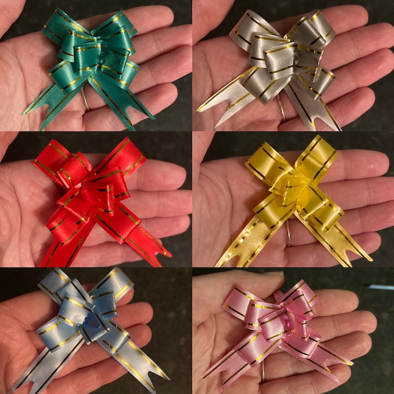 May include: Six different colors of gift bows with gold trim. The bows are made of satin ribbon and have a loop in the center. The bows are arranged in a grid pattern.