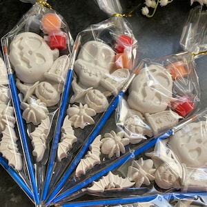 May include: Five clear plastic bags filled with Halloween-themed ceramic ornaments and paint. The ornaments include a pumpkin, a skull, a bat, a spider, and a tombstone. Each bag also includes a small paintbrush and two small bottles of paint.