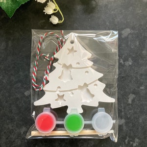 May include: A white ceramic Christmas tree ornament kit with red, green, and silver paint pots and a wooden paintbrush. The kit includes a string for hanging the ornament.