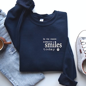 May include: Navy blue sweatshirt with the text "be the reason someone smiles today" and a small white flower graphic.