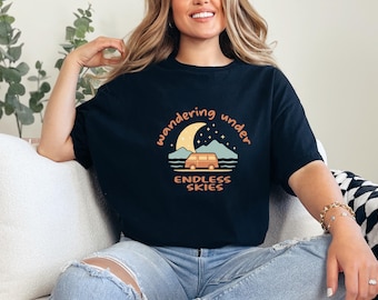 Op de afbeelding: Zwart T-shirt met een afbeelding van een busje dat onder een halve maan met sterren rijdt. De tekst "wandering under endless skies" staat op het shirt gedrukt.
