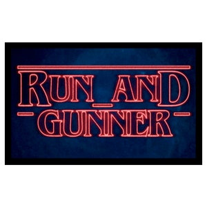 May include: A rectangular sign with the words "RUN AND GUNNER" in red, outlined letters. The text is set against a dark blue background, with a black border. The font style is reminiscent of a retro aesthetic.