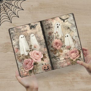 May include: A decorative journal featuring a vintage design with white ghost figures, pink roses, and a jack-o'-lantern. The journal has a distressed look with a spiderweb in the upper left corner. The pages have a musical note and script background.
