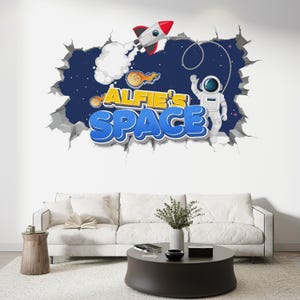 May include: A wall sticker with a rocket, astronaut, and the text "ALFIE'S SPACE". The design gives a 3D effect of a hole in the wall, showing a starry space scene. The text is in blue and yellow.