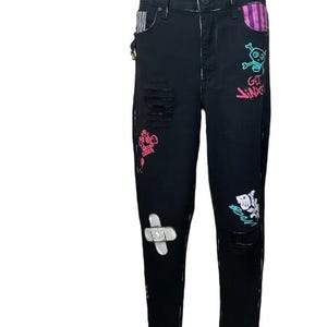 Puede incluir: Vaqueros de mezclilla negros con detalles desgastados y parches decorativos. Los vaqueros presentan un gr&aacute;fico de calavera y huesos cruzados con el texto "GET JINXED", junto con otros dise&ntilde;os coloridos y tachuelas doradas.
